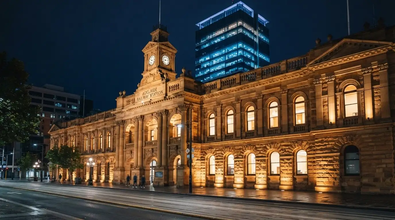 The sandstone façade of the original Adelaide railway station by night, lit from below, with the North Terrace street frontage visible